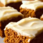 Old-fashioned pumpkin bars topped with cream cheese frosting on a wooden table