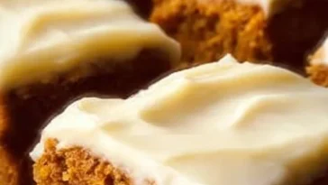 Old-fashioned pumpkin bars topped with cream cheese frosting on a wooden table