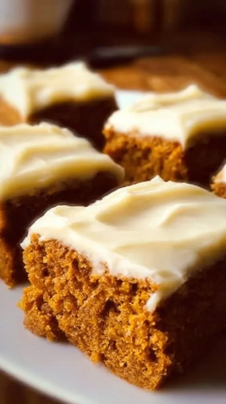 Old-fashioned pumpkin bars topped with cream cheese frosting on a wooden table